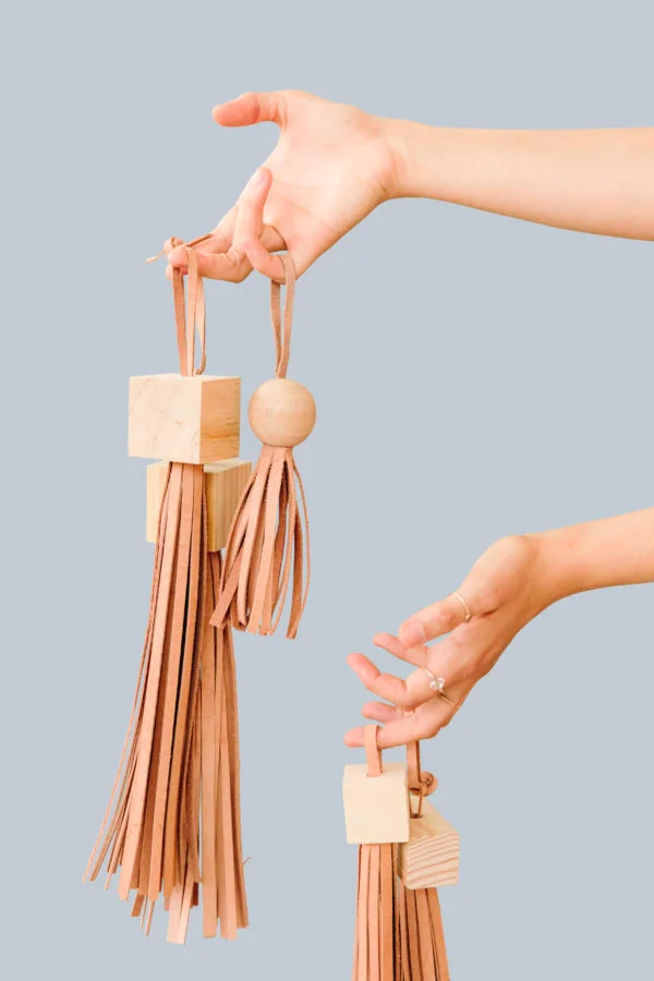 woman holding wood and leather diy tassels with blue background