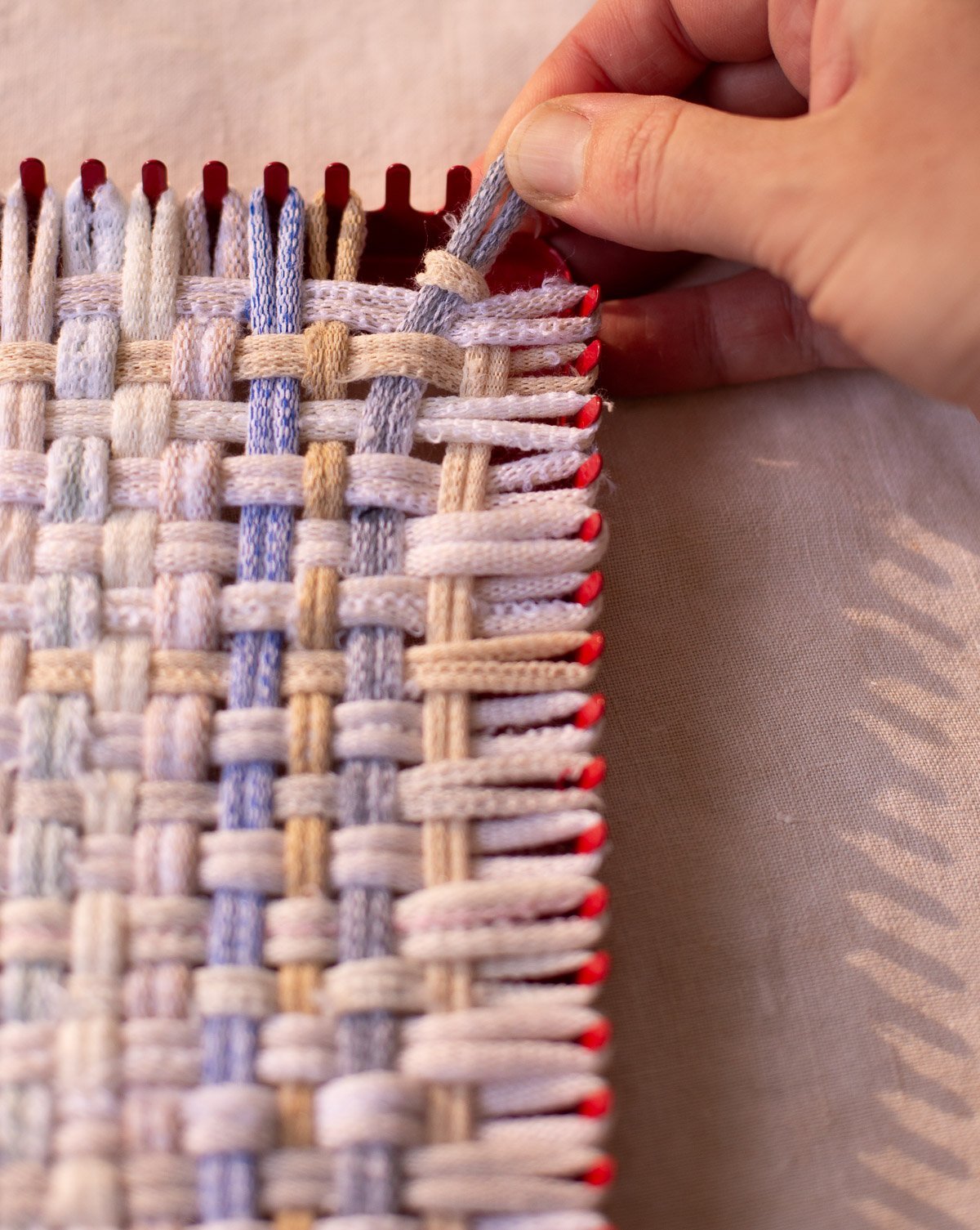 woman finishing a weaving with her hands on small square loom