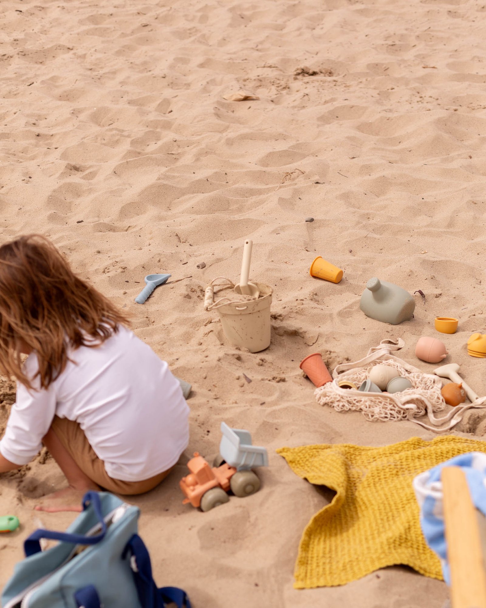child playing in sand at beach with colorful toys